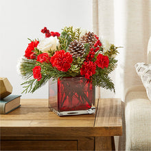 Load image into Gallery viewer, Holiday flower arrangement with red carnations, white roses, pinecones, berries and evergreens in a red glass cube vase
