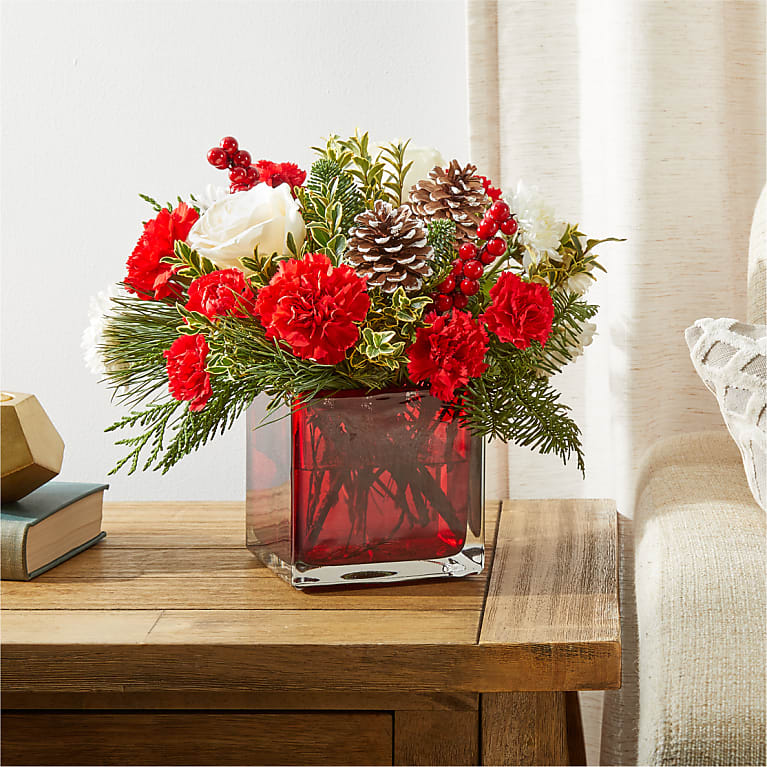 Holiday flower arrangement with red carnations, white roses, pinecones, berries and evergreens in a red glass cube vase
